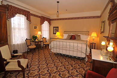 hotel room with king bed two windows with curtains chairs tables and lamps
