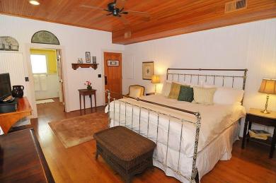 cottage bedroom with iron bed white comforter harwood floors with table dresser and entrance to bathroom