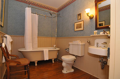 hotel bathroom with shower tub toilet sink chair mirror on wall with pictures and blue wallpaper