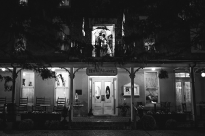 black and white image of Bride and Groom kissing on second story porch holding an umbrella