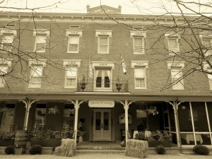 sepia tone exterior of brick hotel during winter with flags hay pumpkins and chairs